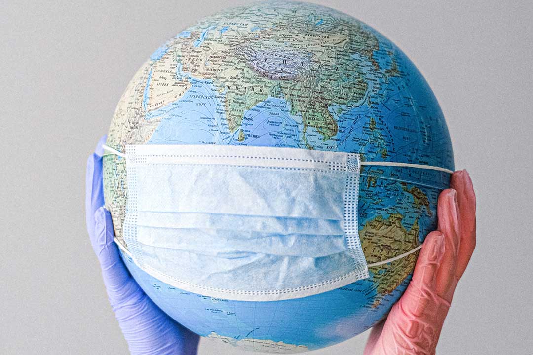 Gloved hands holding a globe with a face mask. Credit: Anna Shvets on Pexels