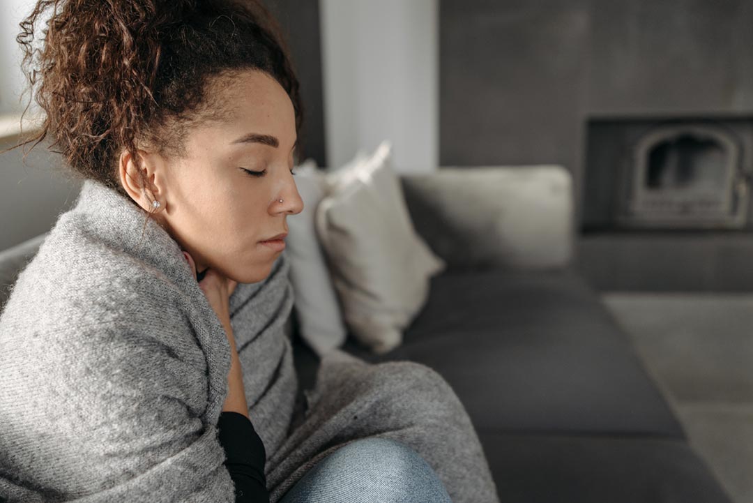 A woman in a blanket holding her hand against her throat. Credit: Pavel Danilyuk on Pexels