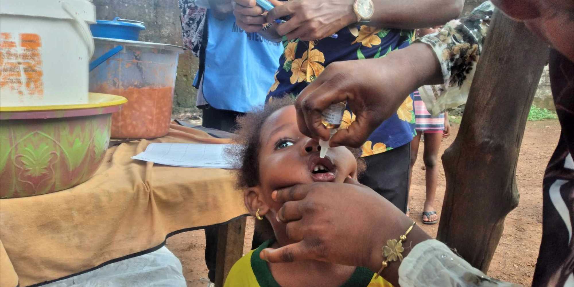 Un enfant reçoit une dose de vaccin contre la polio à côté de sa maman vendeuse de haricots à Dabompa, Conakry. Crédit : Alpha Abdoullaye Diallo