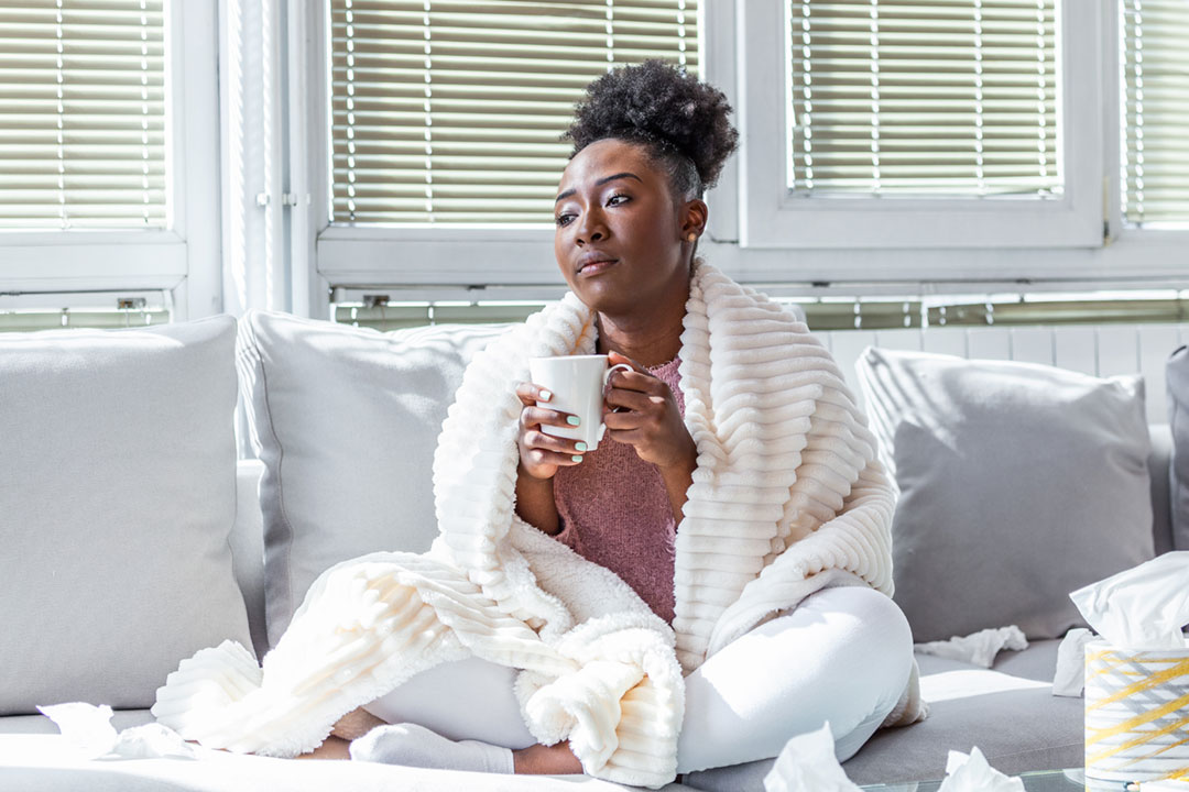 Sick woman sitting on a couch at home with a cup of tea.
