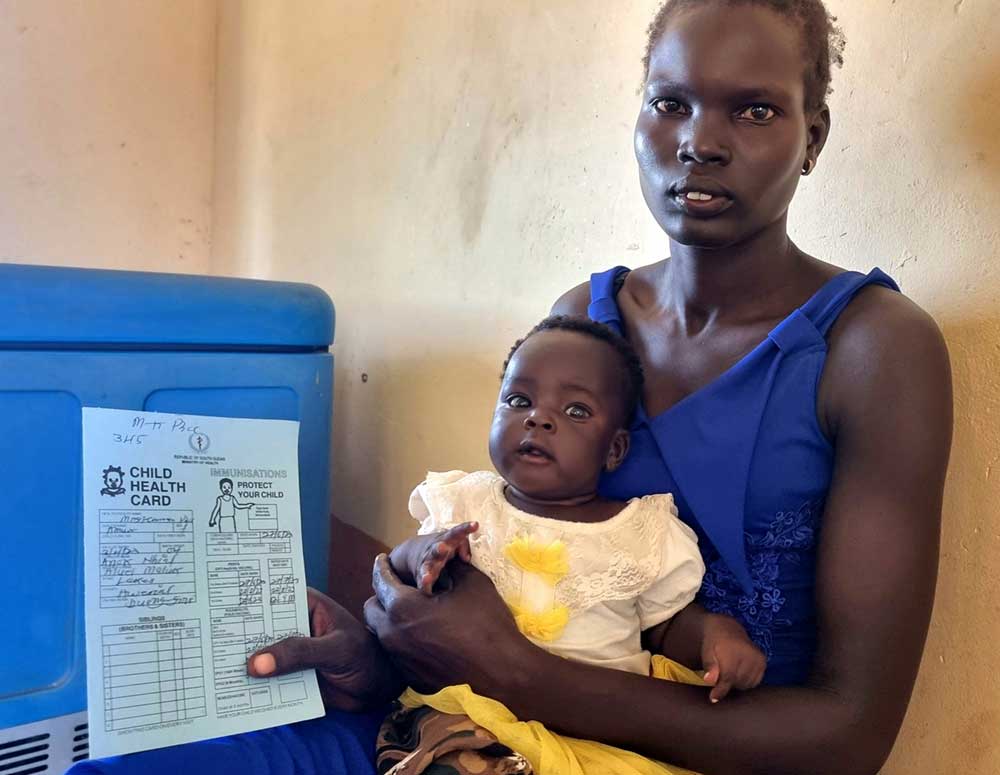 A mother poses for a photo with a child and the vaccination card. Credit: Winnie Cirino