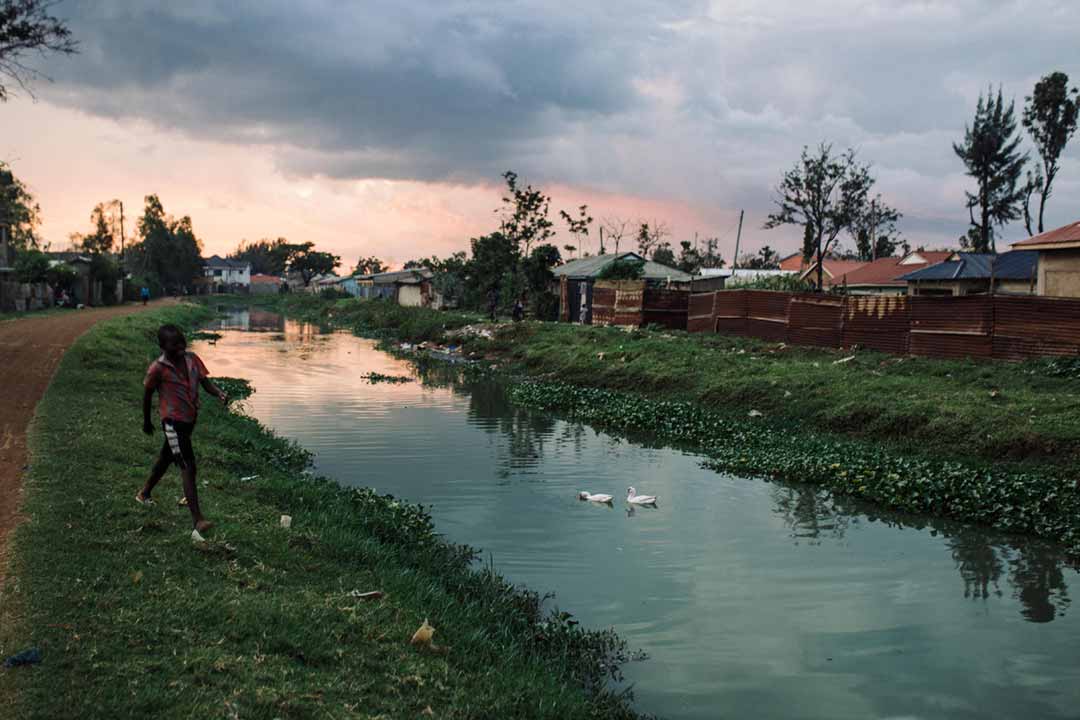 A boy running by the river Auji Wigwa, which runs through Nyalenda slums. The waterway is clogged with the invasive water hyacinth (Eichhornia crassipes) and a known breeding site for mosquitoes. Credit: Kang-Chun Cheng