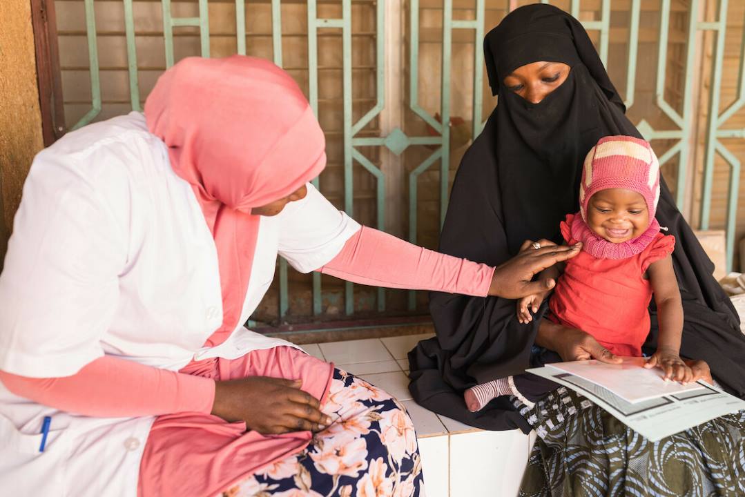 Un bébé joue avec sa mère et un agent de santé au CSI Nouveau Marché, un centre de santé à Niamey, au Niger.