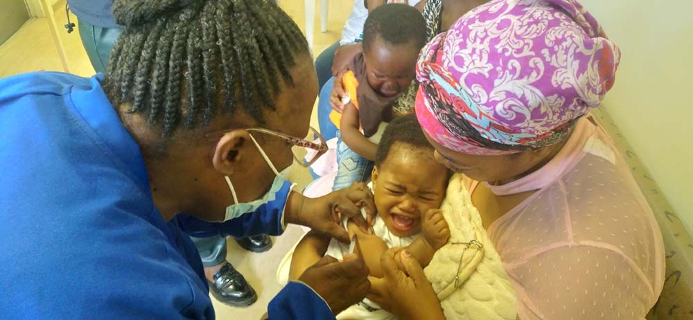 A nurse at Paki Health Centre administers a measles vaccine to a 11-month-old son while his mother, 'Matlhokomelo Mohale, holds him in her arms. Credit: Pascalinah Kabi