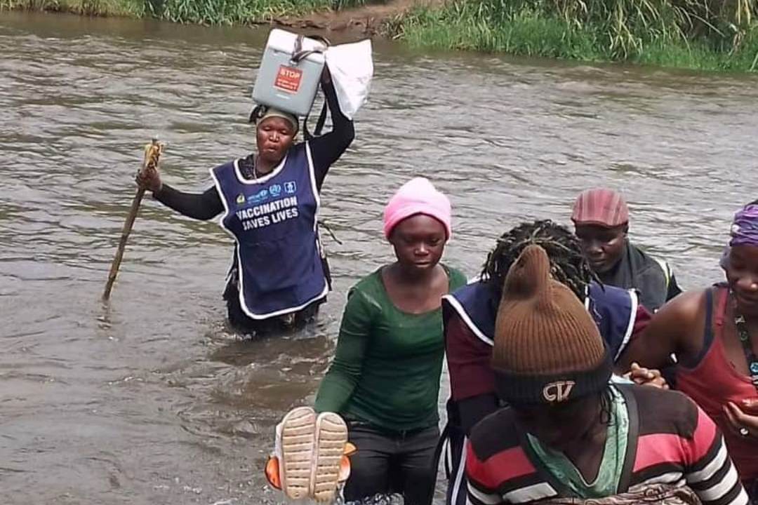 Agent de santé communautaire portant une glaciaire remplie de vaccins traverse un cour d'eau à pied