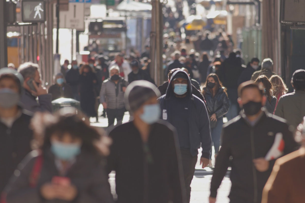A man wearing a facemask walks along a crowded city street.
