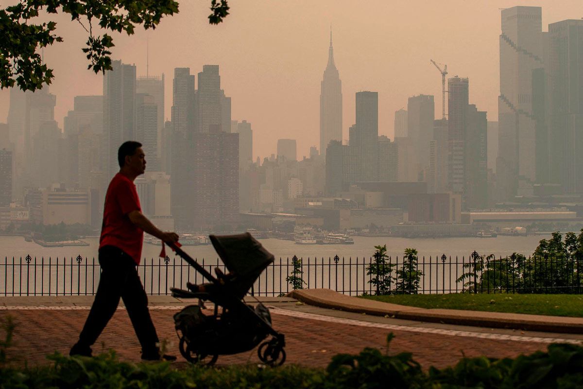 A person walks with a stroller in a park in front of the New York City skyline in June 2023 as it’s covered with haze and smoke from Canada wildfires. Visual: Eduardo Munoz Alvarez/Getty Images