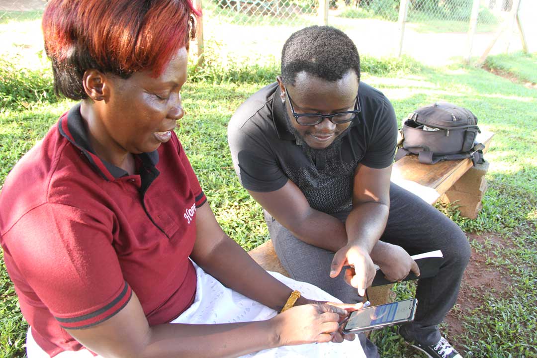 Andrew Ddembe, co-founder of MobiKlinic discusses the app with Dorothy Kirunda, a CHW from Kiyindi Town Council. Credit: James Karuga