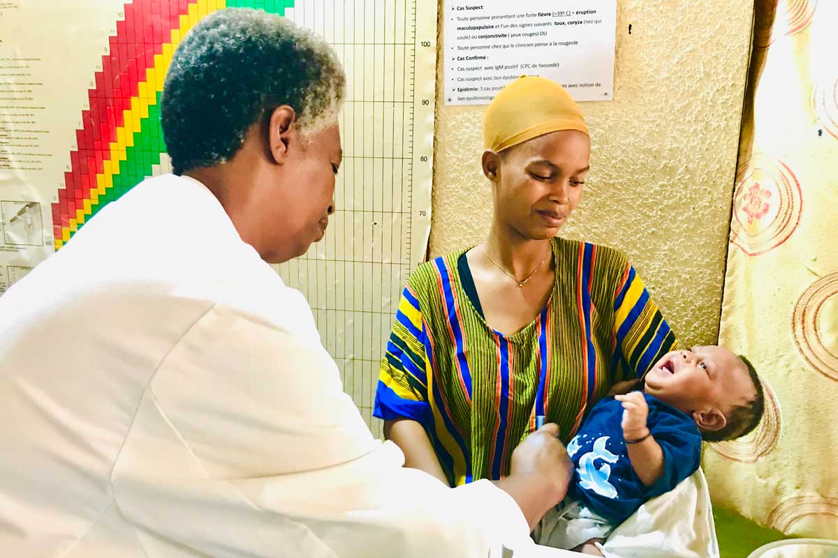 A mother holds her child while a nurse administers the measles vaccine. Credit: Moses Havyaramina