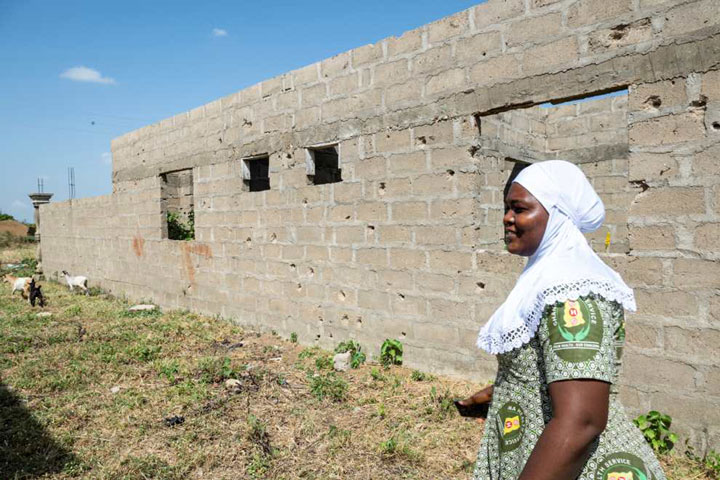 Hamidu Hikmatu, the nurse in charge of the Patelmi CHPS centre, walks past a wall riddled with bullet holes at the back of the health facility. Credit: Claudia LaCave/Hans Lucas