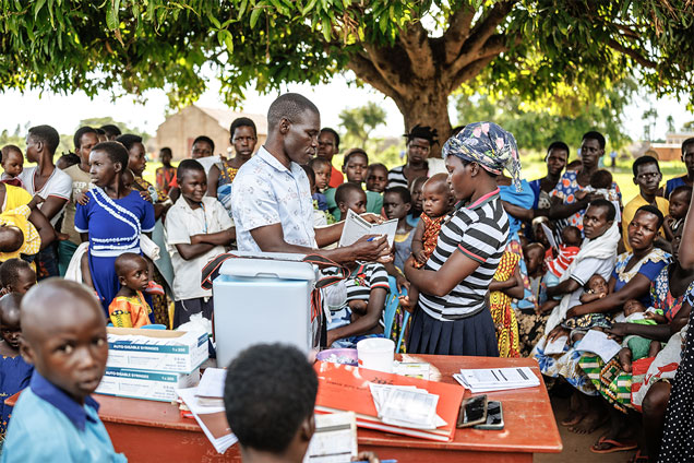 During a community outreach session on the grounds of a school in Apac district, a health worker emphasises to a mother that the R21/Matrix-M vaccine is administered in four doses, at 6, 7, 8, and 18 months of age.