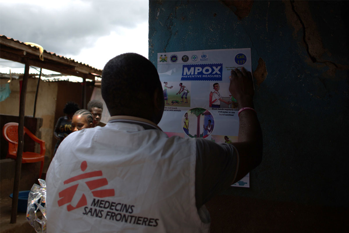 An MSF Health Promotion and Community Engagement team member paste  an mpox awareness  poster on a wall in the Calaba Town community in Freetown. Credit: Saidu Bah