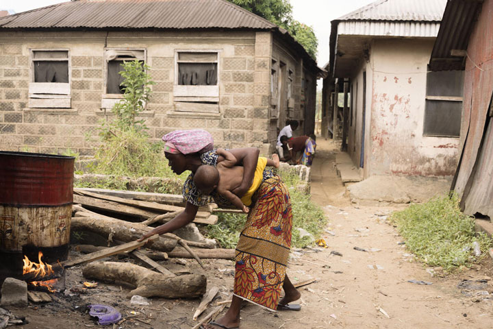 Permanent Aselo, 23 years old, holding her son Talent next to her house in the Onuegbu community, Bayelsa State, where she sells grilled fish. Ogbia, Nigeria. December 17, 2024. Credit: Jérôme Sessini