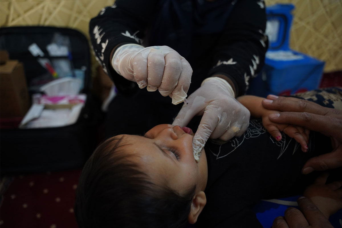 A health worker administers oral vaccine drops to Jameel’s child inside his family's temporary shelter. Credit: WHO
