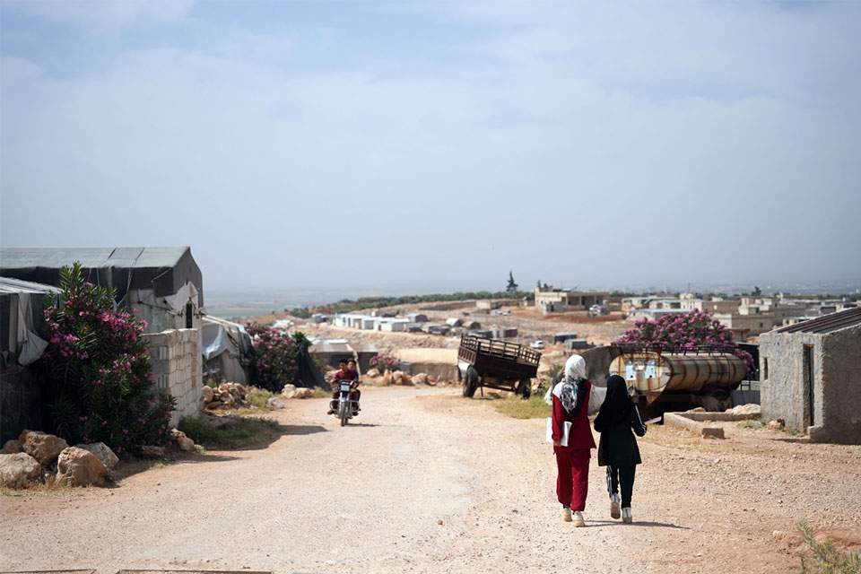 Two health workers walk through Al-Burj camp in Idlib, going tent to tent to ensure children are protected through routine vaccination. Credit: WHO