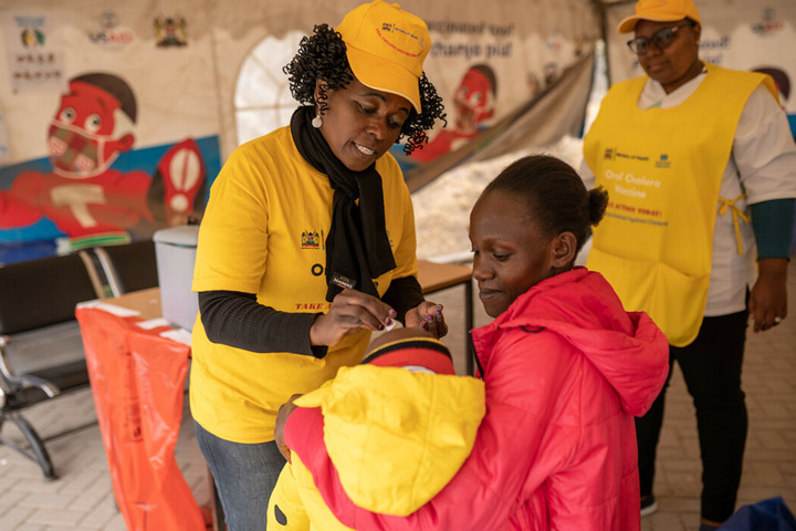 Janet Maloba, 27, holds her son as he receives the Oral Cholera Vaccine at vaccination facility. August 10th, 2023. Kajiado East, Kenya. Credit: Gavi, Kelvin Juma