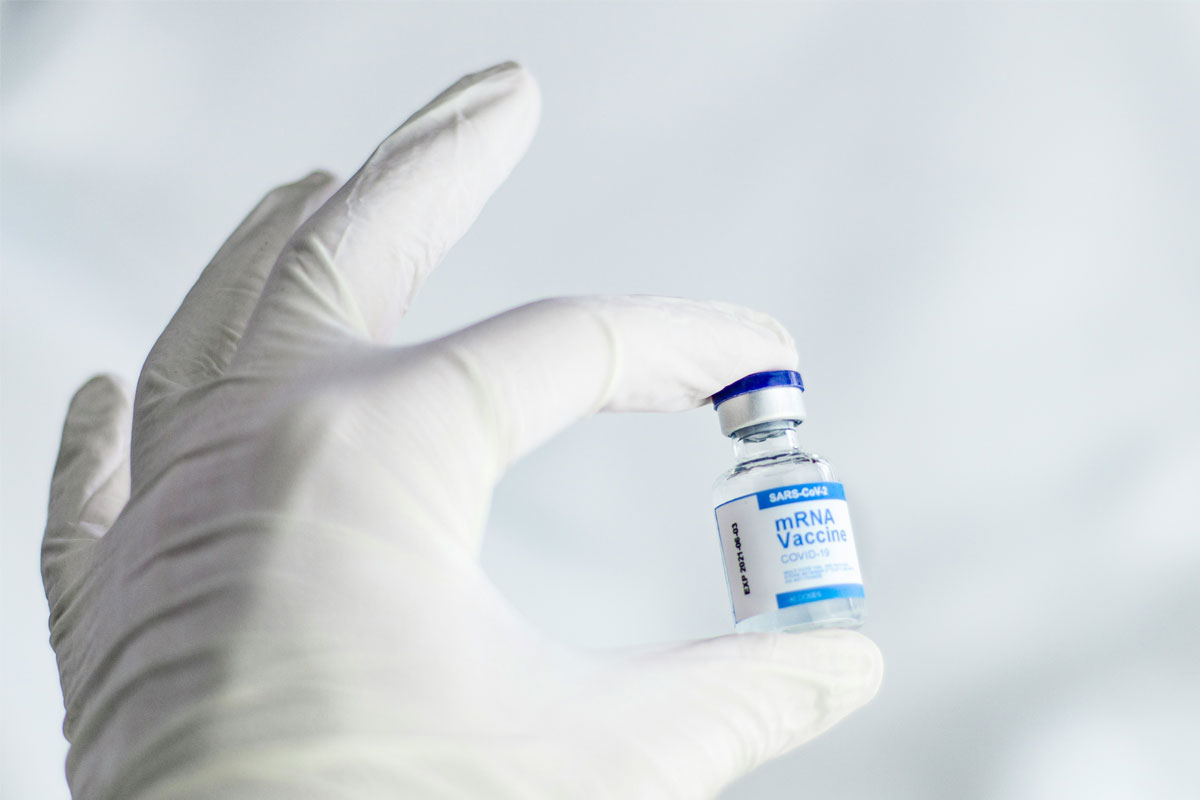Close-up of a hand holding a blue and white vial of an mRNA-based COVID-19 vaccine. Credit: Spencer Davis on Unsplash