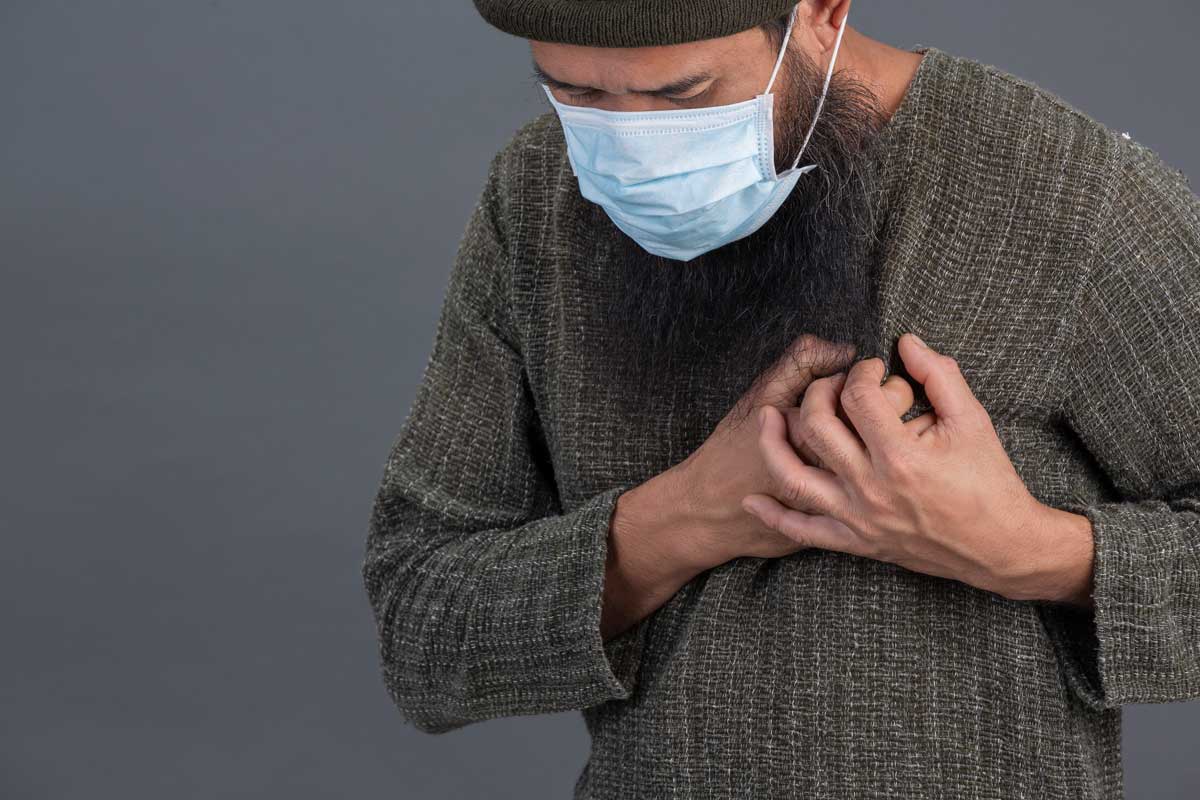 A man wearing a facemask holds his chest. Credit: jcomp on Freepik