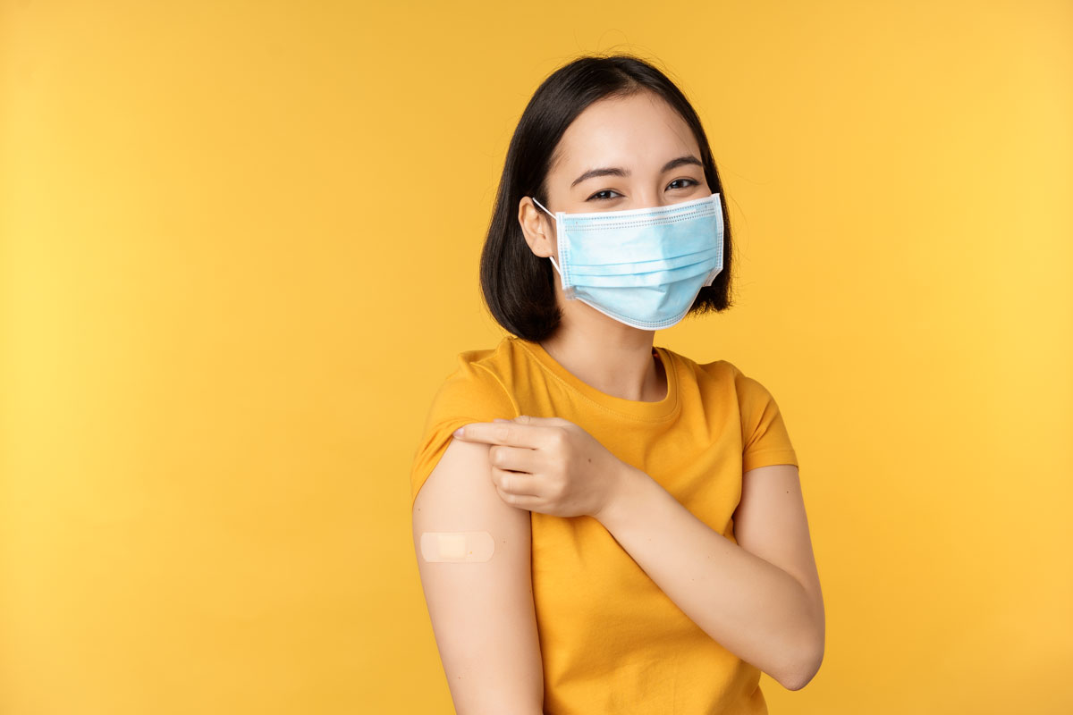 A smiling woman wearing a medical face mask showing her shoulder with band aid after being vaccinated. Credit: Benzoix/Freepix