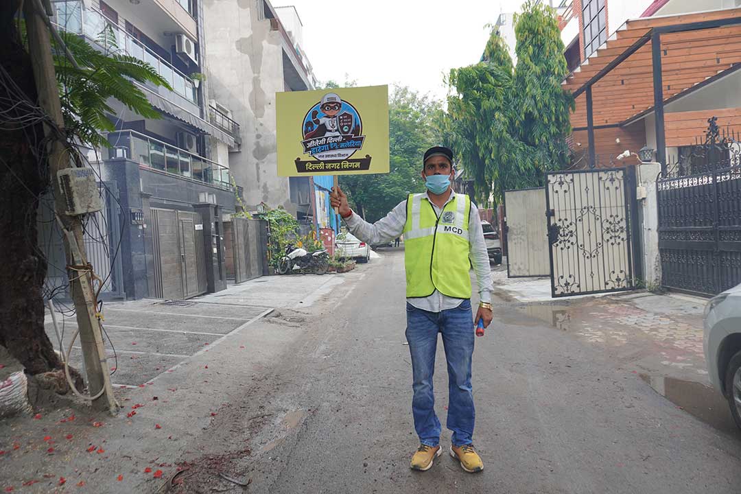 A Municipal Corporation of Delhi worker conducts a dengue awareness campaign in a South Delhi neighborhood, using illustrated signboards to communicate prevention measures to residents, including those with limited literacy. Credit: Safina Nabi