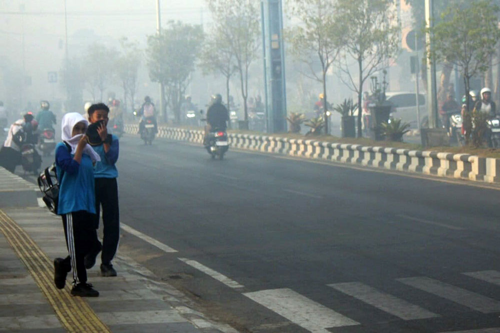Two students cover their noses as they head to school to avoid exposure to the smoke from forest and land fires that blanketed the Martapura area. Image by Riyad Dafhi Rizki/Mongabay Indonesia.