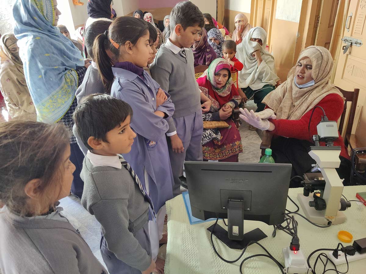 A female health worker demonstrates proper handwashing techniques to children and their mothers after showing them live germs under a microscope in samples brought from their homes. Credit: Development Synergies International.