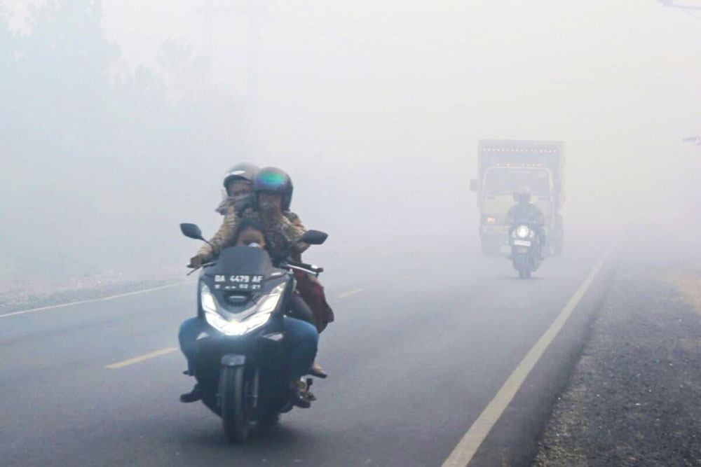 Commuters on the road try to shield their noses from the thick haze as they drive. Image by Riyad Dafhi Rizki/Mongabay Indonesia.
