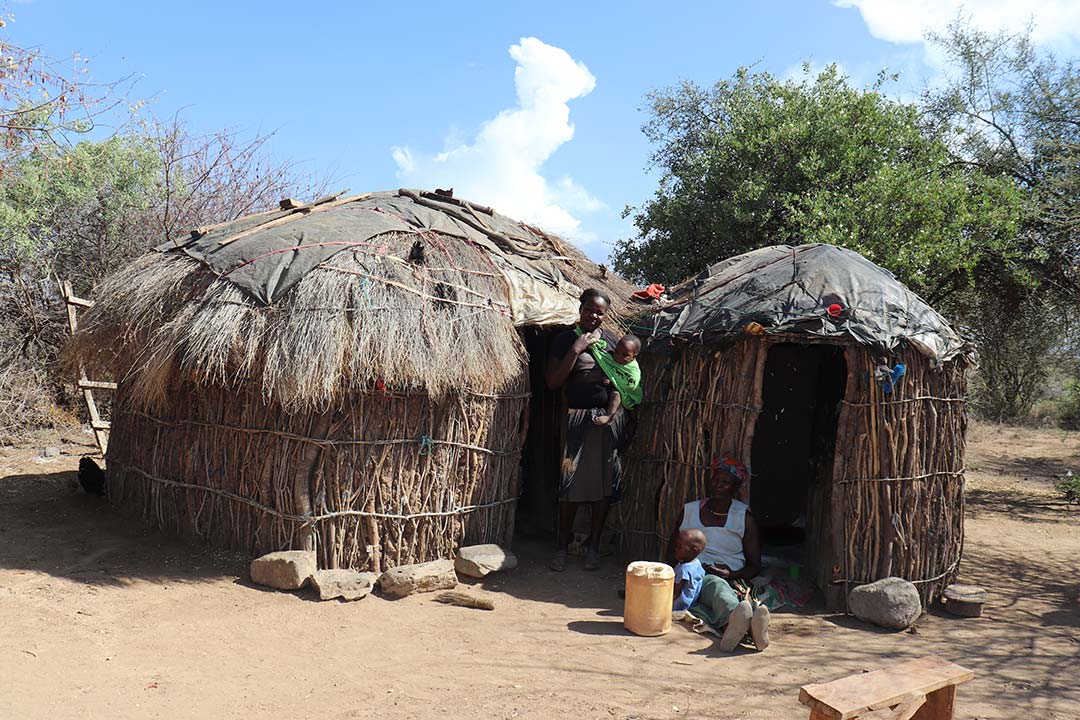 Angelina Muthoni stands outside their hut in Aremet with her mother sitting enjoyng the house's shade with her other child. Credit: Dominic Kirui
