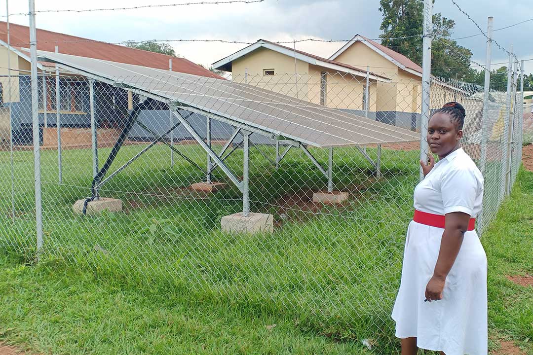 Betty Nakazibwe with the 12KW solar power panels that supply the facility and staff quarters. Credit: John Musenze