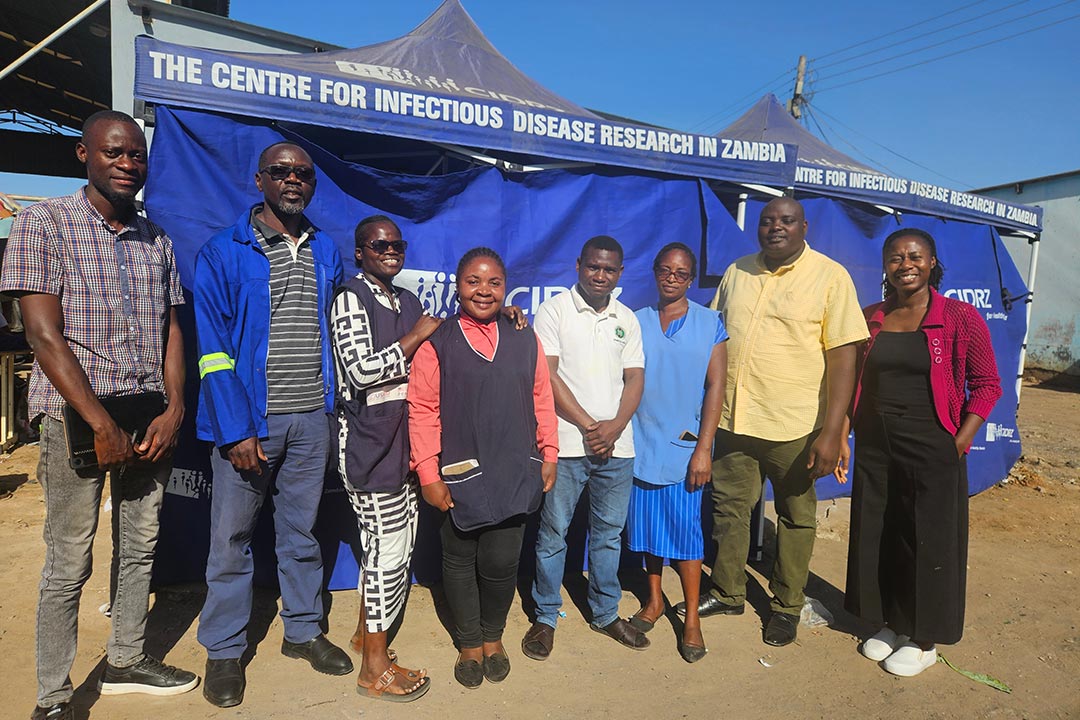 Dr Seke Muzazu, in a pink sweater over black, stands on the far right with part of the data collection team at a community field station. Credit: Seke Muzazu