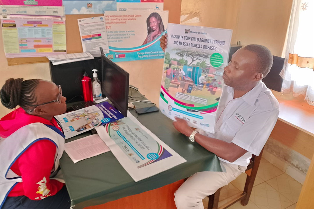 Peter Abwao, PATH’s Communications Lead in Kenya, discusses typhoid and measles vaccines with a local health worker. Credit: PATH