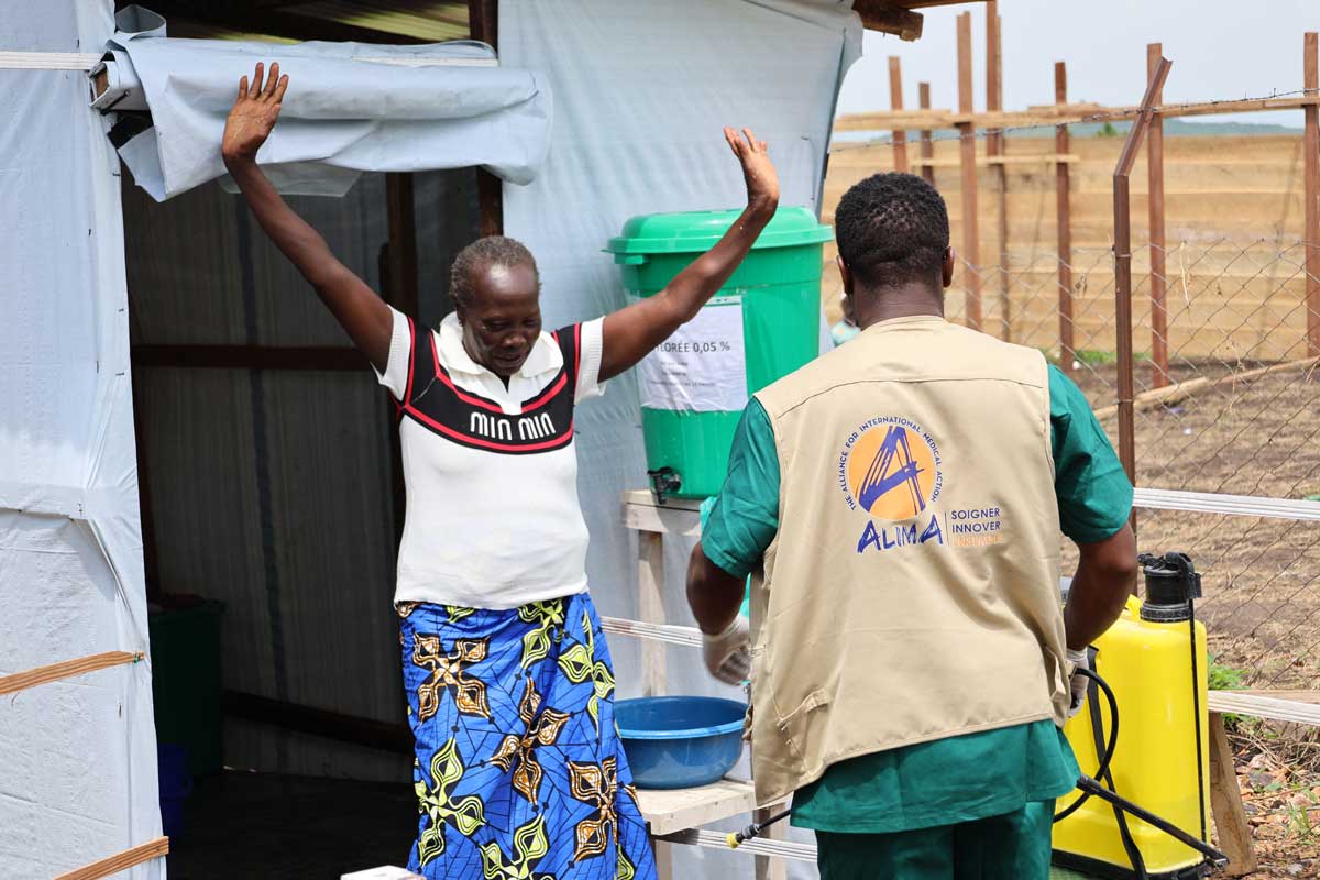 Leaving the disinfection zone at the Rwampara Ebola Treatment Center run by ALIMA, a 66 y.o. woman expresses her immense joy and bids a final 'goodbye' to Ebola virus disease. This triumphant gesture reflects her satisfaction with the successful care she received and her rebirth following a period of intensive treatment. June 2026. Photo credit: Elie BIGABA / ALIMA