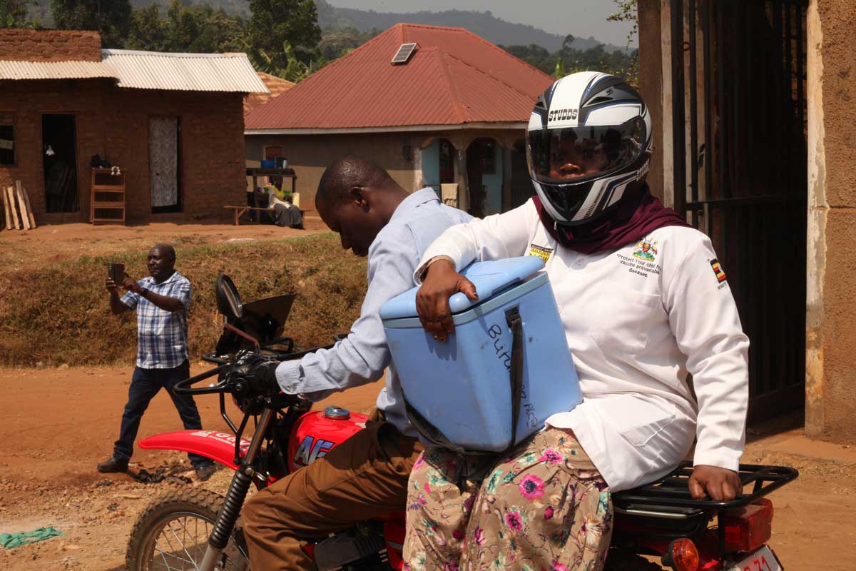 Zaina Namalwa, an enrolled nurse and immunisation focal person going to a second outreach, being riden by a hospital nursing officer. Credit: John Musenze