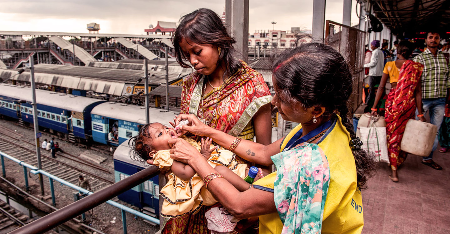 A health administers an oral polio vaccine to a child in an Indian railway station